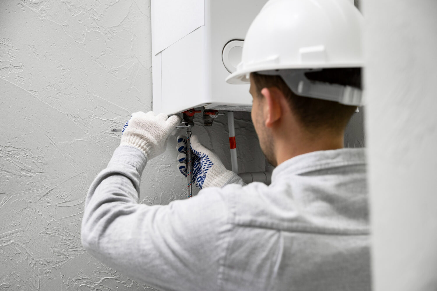 Técnico instalando calentador de agua en pared con casco de seguridad.